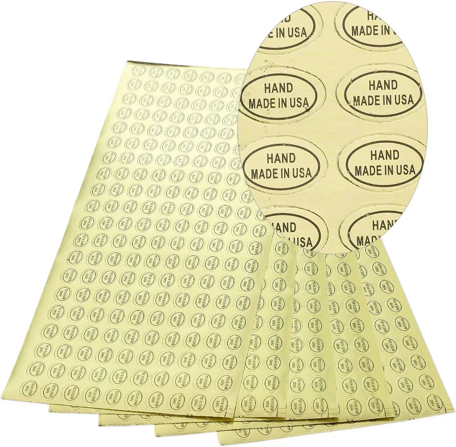 Adhesive label, paper, gold and black, 1/2 x 5/16 inch oval with "HAND MADE IN USA." Sold per pkg of 1,000. | Fire Mountain Gems and Beads